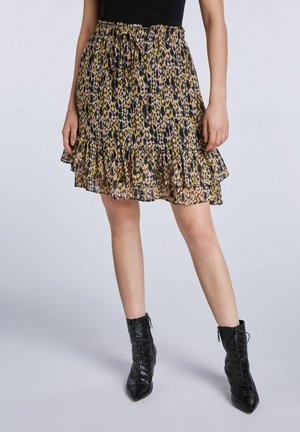 Femme portant une jupe à volants imprimée léopard avec une taille à cordon et des bottines noires à lacets, debout devant un fond uni.