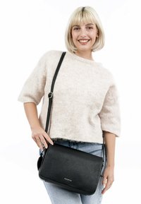 Bolso cruzado de cuero negro con un acabado texturizado, forma rectangular, correa ajustable y un simple detalle de hardware plateado.