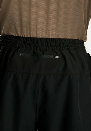 Črne lahke kratke hlače z elastičnim pasom. Imajo majhen žep z zadrgo na hrbtu, izdelane so iz teksturirane, zračне tkanine.