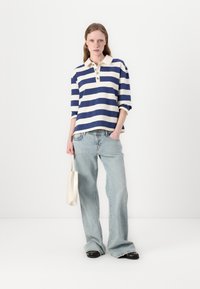 Navy and cream striped polo shirt with a collar and three buttons, paired with light blue wide-leg jeans and a cream bag.