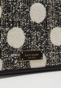 Borsa a mano in tessuto nero e bianco con una texture e grandi pois bianchi. Presenta una placca dorata con "kate spade NEW YORK" e dettagli neri.