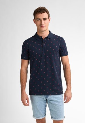 Polo navy con piccoli motivi rossi, maniche corte e colletto con bottoni, abbinato a pantaloni corti azzurri arrotolati.