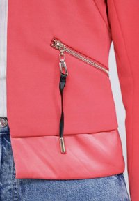 Veste zippée corail en tissu texturé, avec une fermeture éclair argentée et un tirette noire, design en couches et une partie inférieure en satin lisse.