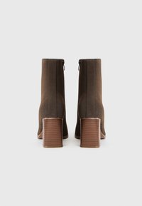 Paire de bottines en daim marron vues de dos, avec talons blocs en bois empilés et fermetures éclair latérales sur un fond clair.