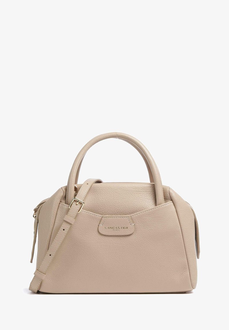 Sac à main en cuir beige avec une forme structurée, deux anses supérieures et une bandoulière amovible. Présente un accent de logo doré et des détails zippés.