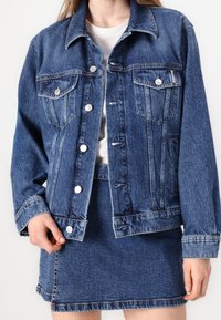 Mörk denimjacka med klassisk krage, framtida knappstängning, två bröstfickor och långa ärmar, med en något oversized passform.