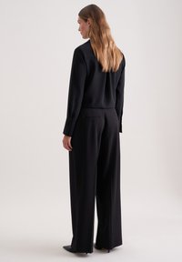 Zwarte lange mouwen top met een gladde textuur, gecombineerd met wijde zwarte broek met achterzakken en knoopaccenten.