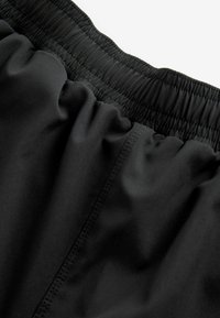 Sorte atletiske shorts med elastisk talje, glat struktur, samlede syninger og et enkelt design, der viser stofholdbarhed.