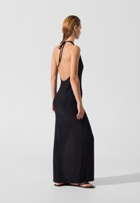 Mustast sädelevast kangast valmistatud madala seljaga must halterkaelusega maksikleit. Omab kitsast lõiget ja küljes lahku, sobitub lameda tallaga sandaalidega.