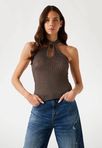 Hnědý žebrovaný pletený halter top s výstřihem ve tvaru klíčové dírky na dekoltu, v kombinaci se sepranými modrými kalhotami s širokými nohavicemi.