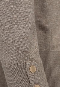 Garen trui in taupe met een gladde textuur; heeft gouden knoopaccenten op de mouw en een aansluitend manchetontwerp.