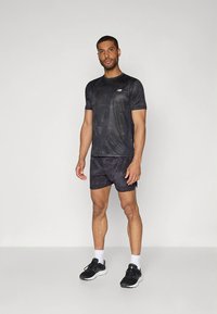 Svart sport-t-shirt med ett subtilt mönster, kombinerad med mörka shorts. Bärs med svarta löparskor och vita ankelstrumpor.