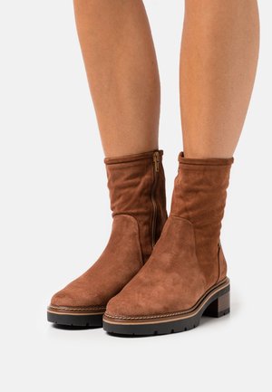 Brown suede ankle boots with a folded top, side zipper, and a chunky heel. Features a smooth texture and contrasting stitching detail.