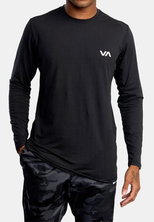 Long-sleeve black shirt made of smooth fabric, featuring a white logo on the left chest. Worn with camo-patterned black shorts.