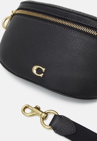 Zwarte leren crossbody tas met een gestructureerd oppervlak, gouden rits en een gouden logo-accent. Bevat een afneembare schouderband met een haak.