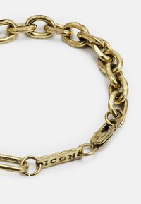 Pulseira de corrente em metal dourado com um design de grandes elos e fecho de mosquetão. Apresenta uma etiqueta gravada "ICON" perto do fecho.
