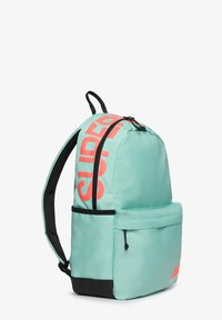 Mochila de color turquesa claro con base y correas negras, gran texto en color coral rojo "SUPER" en un lado, bolsillo con cremallera en la parte frontal y cierre de cremallera en la parte superior.