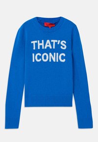Blå strikkegenser med ribbede mansjetter og kant. Har hvit tekst som sier "THAT'S ICONIC" fremtredende på fronten. Myk tekstur.