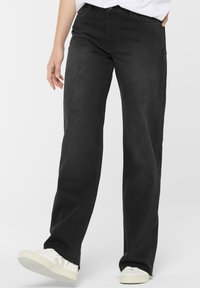 Schwarze Denim weit geschnittene Hose mit hoher Taille, fünf Taschen-Design und gesteppten Nähten. Kombiniert mit weißen Sneakers für einen Kontrast.