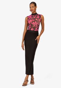 Schwarze, figurbetonte Skirt kombinierte mit einem transparenten, floral gemusterten Oberteil in Pink und Schwarz. Ärmelloses Design mit hohem Hals. Inklusive High Heels.