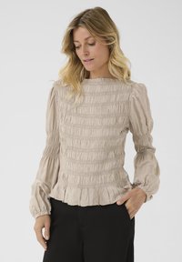 Blusa in cotone beige con arricciatura, maniche lunghe a sbuffo e orlo arricciato, caratterizzata da un tessuto testurizzato e un collo rotondo.