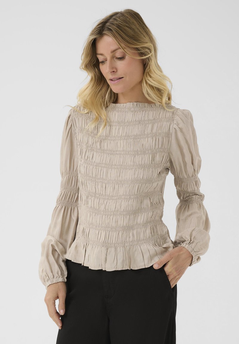 Blusa in cotone beige con arricciatura, maniche lunghe a sbuffo e orlo arricciato, caratterizzata da un tessuto testurizzato e un collo rotondo.