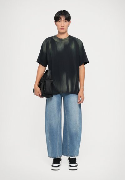 Must värvi ülerõhu särk, millel on rohelise batikakujundusega musta värvi, koos heleda sinise kaotatud lõikega denimipükstega ja mustade tossudega. Käes must kott.