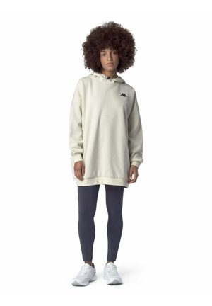 Felpa crema oversize con logo nero sul petto, abbinata a leggings grigio scuro e sneakers bianche. Tessuto liscio, vestibilità casual.