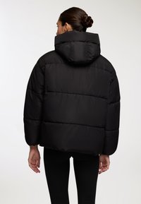Czarna kurtka puchowa z kapturem, o pudełkowym kroju, puszystej fakturze i ściągaczach na rękawach, widziana z tyłu.