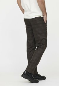 Braun gestreifte Hose mit einer schlanken Passform, die subtile orange und beige Linien aufweist, und ergänzt durch schwarze Schuhe mit einer dicken Sohle.