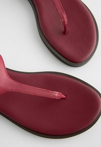 Punaiset nahka flip-flop-sandaalit, joissa on ohut thong-hihna ja pehmeä pohja, varustettu kontrastilla mustalla kumipohjalla. Tasainen pinta koko matkalta.