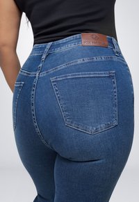 Donkerblauwe spijkerbroek met hoge taille, voorzien van een leren label aan de achterkant, vijf zakken en een getailleerd silhouet.