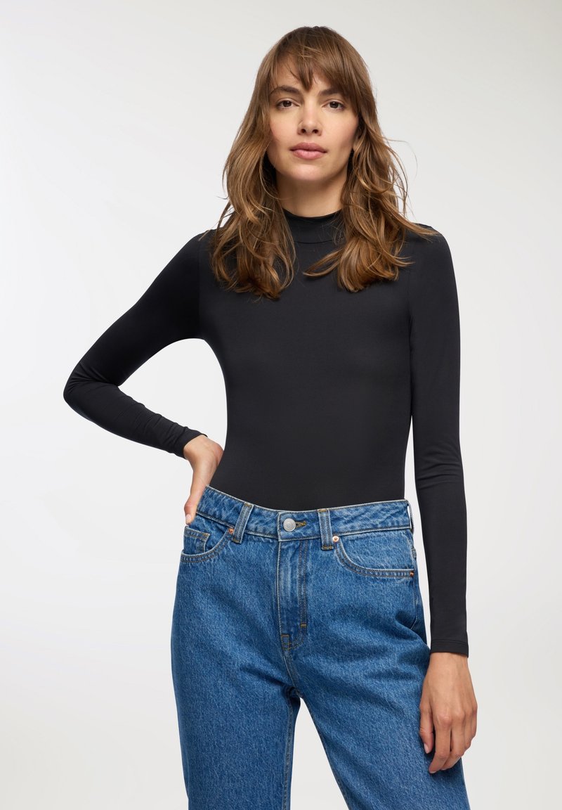 Body nero a maniche lunghe abbinato a jeans in denim blu a vita alta. Il body presenta una texture aderente e liscia.
