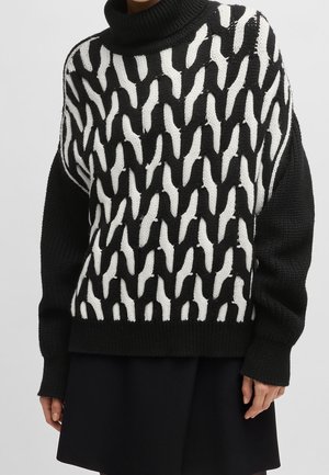 Sort-hvid chunky strikket sweater med abstrakt mønster, lange ærmer og høj rullekrave båret over et sort skørt.
