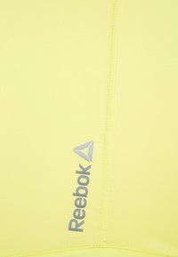 Gul Reebok-tanktopp med en mjuk textur, en figurnära design och en framträdande silverlogotyp på vänster sida.