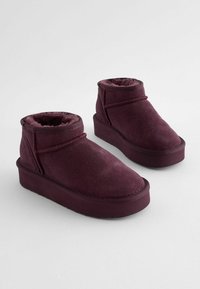 Bottines bordeaux avec un extérieur en daim doux, un intérieur douillet, et une semelle épaisse et texturée avec des détails de couture contrastés.