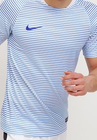 Camisa deportiva Nike a rayas azul y blanca, de manga corta, con un logo azul en el pecho y una tela texturizada y ligera.