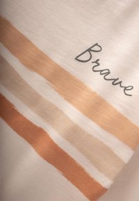 Tessuto di cotone con base beige chiaro caratterizzato da strisce orizzontali a pennellate nelle tonalità pesca e marrone chiaro. "Brave" stampato in grigio scuro.