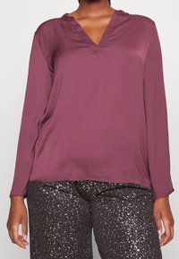 Maglietta a maniche lunghe color bordeaux con scollatura a V, realizzata in tessuto morbido. Abbinata a pantaloni neri con un motivo scintillante dorato.