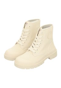 Beige canvas ankle boots with round toes, lace-up front, ribbed rubber soles, and a circular logo detail on the outer side.