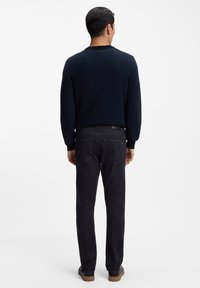 Suéter de cuello redondo en azul marino oscuro con tela texturizada, combinado con jeans gris oscuro y zapatos negros. Diseño sencillo con puños y dobladillo acanalados.