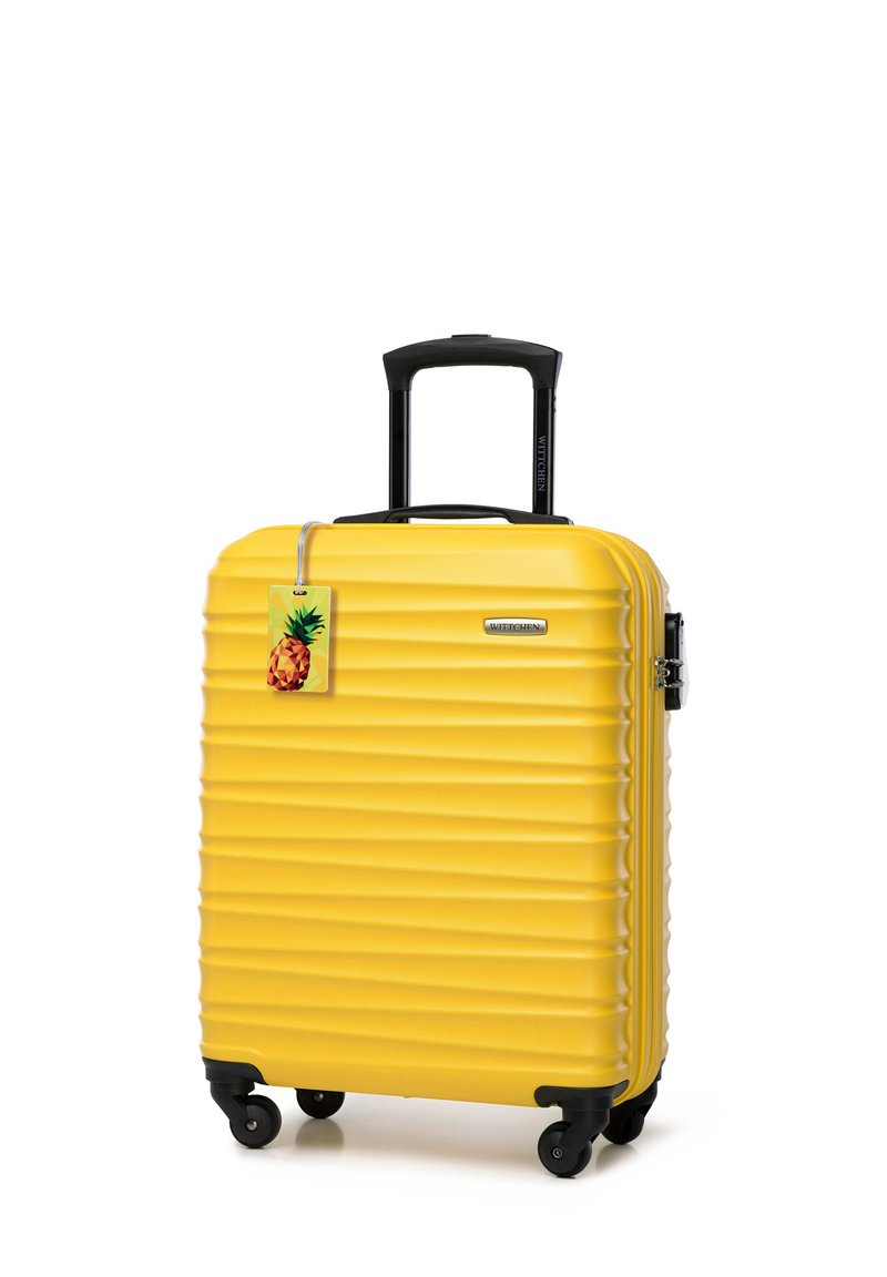 Maleta amarilla de carcasa dura con textura estriada, mango retráctil negro y ruedas. Incluye una etiqueta con un gráfico de piña.
