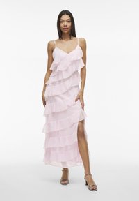 Svetlo roza maxi obleka z večplastnimi ruffles, nastavljivimi naramnicami in stranskim razporkom. Narejena iz prosojne, lahkotne tkanine.