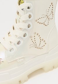 White combat boot made of glossy material with cutout butterfly designs, reinforced eyelets, and a chunky translucent sole.