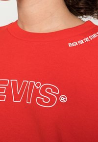 T-shirt rossa in cotone con il logo bianco di Levi's sul davanti e la scritta "REACH FOR THE STARS" stampata in bianco sulla spalla.