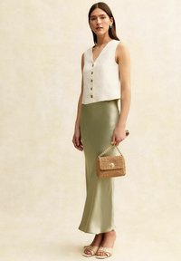 Vit linnetopp utan ärmar med knappar fram, matchad med en ljusgrön satinv skirt och en vävd beige handväska med kedjerem.