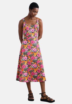Floral dress in pink, orange, and green with a square neckline, wide straps, and flared hem; paired with black strappy sandals.
