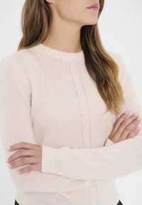 Light pink sweater with a round neckline, textured center panel, ribbed cuffs, and soft knit fabric. Design appears casual and comfortable.