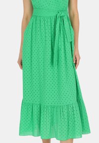 Zielona midi sukienka z teksturowanym wzorem ażurowym, dopasowaną górą, paskiem w talii oraz rozkloszowanym dołem. Lekka tkanina zapewniająca oddychalność.