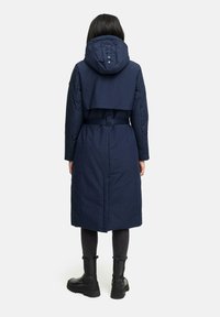Cappotto imbottito blu navy con cappuccio e vita svasata, caratterizzato da un design cropped e una texture liscia, adatto per il freddo.